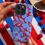 A hand holds a light blue and red floral patterned phone case on an iPhone. The case features a bold, repeating floral design with the brand name 'CASELO' printed near the bottom.