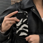 A person wearing a black leather jacket holds a smartphone in a pocket. The phone case has a black and white zebra pattern and the brand name 'CASELO' is printed near the bottom.